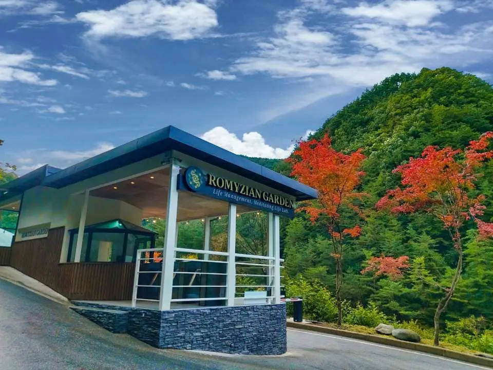Modern entrance building of Romijian Garden on Jeongseon's Gariwang Mountain. A clear park sign and vibrant red-leaf trees welcome visitors to this lush healing forest.