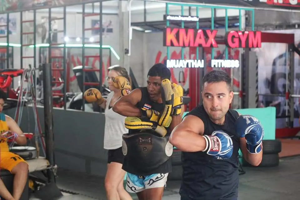 Energetic Muay Thai student practicing punches with a professional instructor holding pads at Kmax Gym in Krabi, Thailand, highlighting the immersive fitness experience.