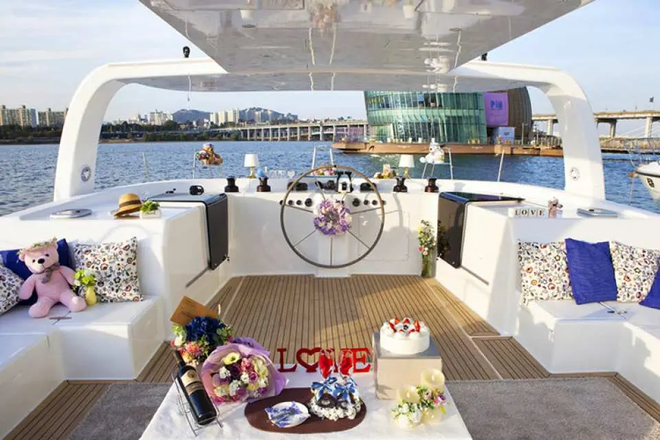 The interior of a luxury private yacht on the Han River is exquisitely decorated with 'LOVE' signs, cake, wine, and flowers, creating a romantic atmosphere perfect for couples' dates or proposals.