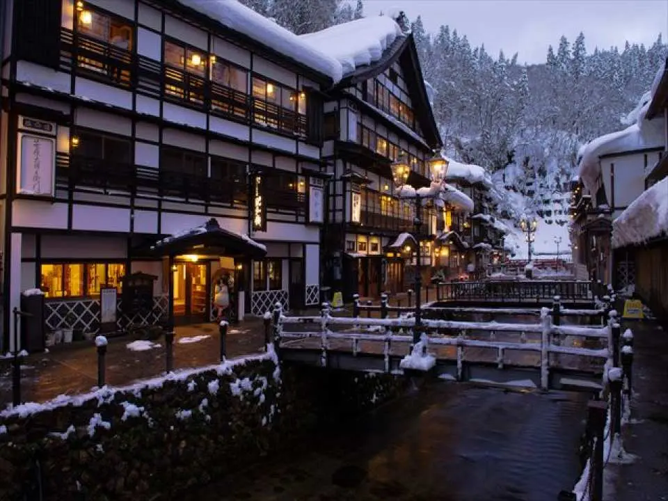 Serene winter twilight at Ginzan Onsen, Yamagata, Tohoku, displaying snow-covered traditional Taisho-era inns and bridges along the hot spring street, perfect for an authentic Japanese cultural experience.