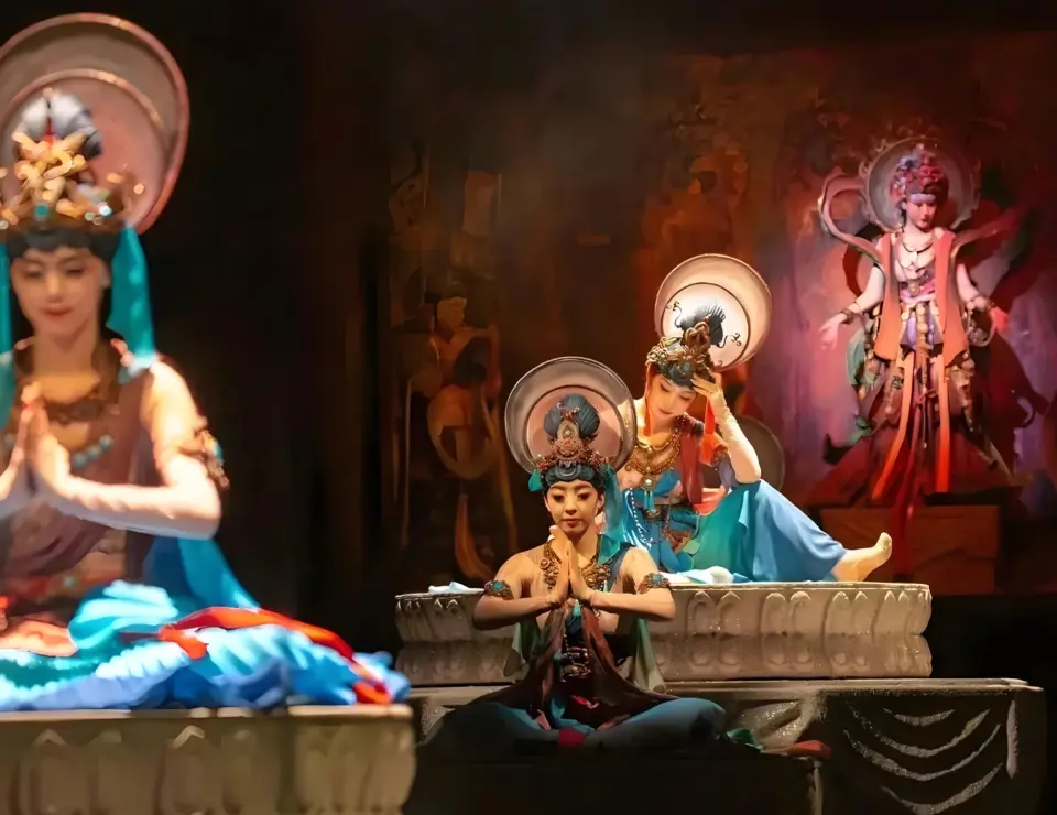 Performers in "Music Moves Dunhuang" immersive show, embodying Dunhuang Bodhisattva figures in exquisite costumes, gracefully dance against a cave backdrop, recreating Mogao Grottoes art.