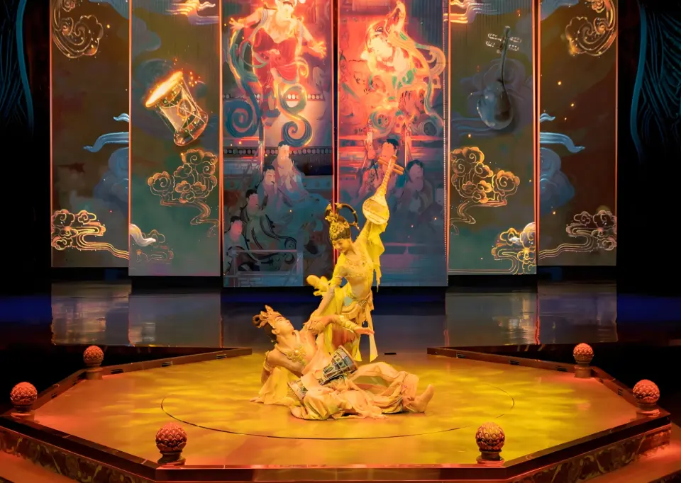 A climax scene in Gansu's "Music Moves Dunhuang" immersive show, where dancers use 3D wirework on a circular stage against dynamic Dunhuang mural projections, telling a Western Regions legend.