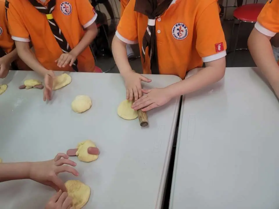 香港多多美麵包廠的烘焙體驗，孩子們的小手正在使用擀麵棍將麵糰擀平，準備製作創意麵包，有的則加入香腸餡料。