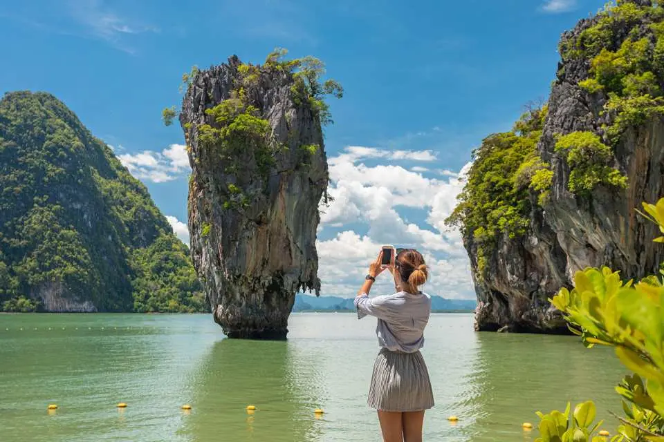 นักท่องเที่ยวถ่ายภาพหน้าเกาะเจมส์บอนด์ (เกาะตะปู) ที่มีชื่อเสียงในอ่าวพังงา ประเทศไทย ชื่นชมแลนด์มาร์คเสาหินปูนอันเป็นเอกลักษณ์และทัศนียภาพอ่าวโดยรอบ