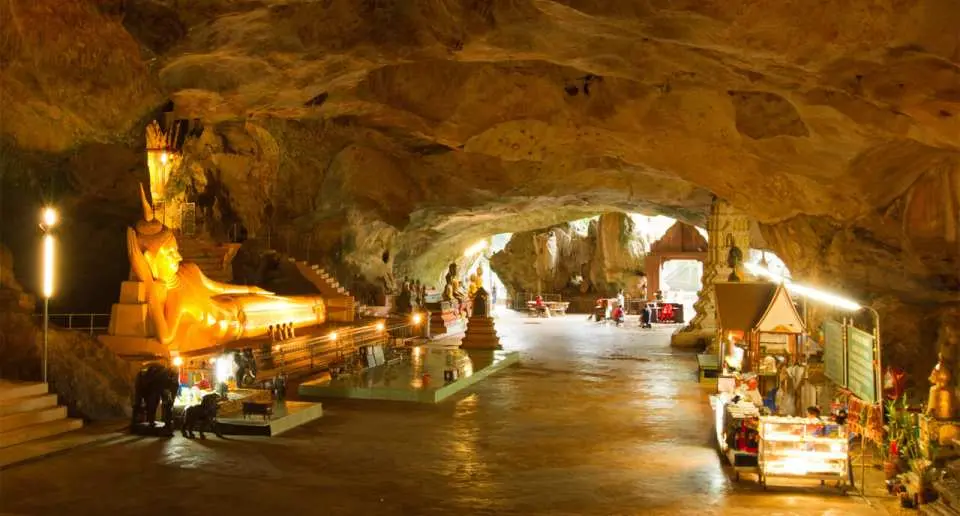 ภายในวัดสุวรรณคูหา (ถ้ำลิง) ในประเทศไทย พระพุทธไสยาสน์สีทองอร่ามขนาดใหญ่เปล่งประกายอยู่ภายในถ้ำ โดยมีนักท่องเที่ยวเยี่ยมชมวัดพุทธโบราณแห่งนี้