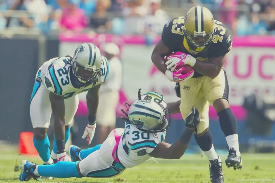 Dynamic action shot of an NFL New Orleans Saints player carrying the football, evading tackles during an intense game.