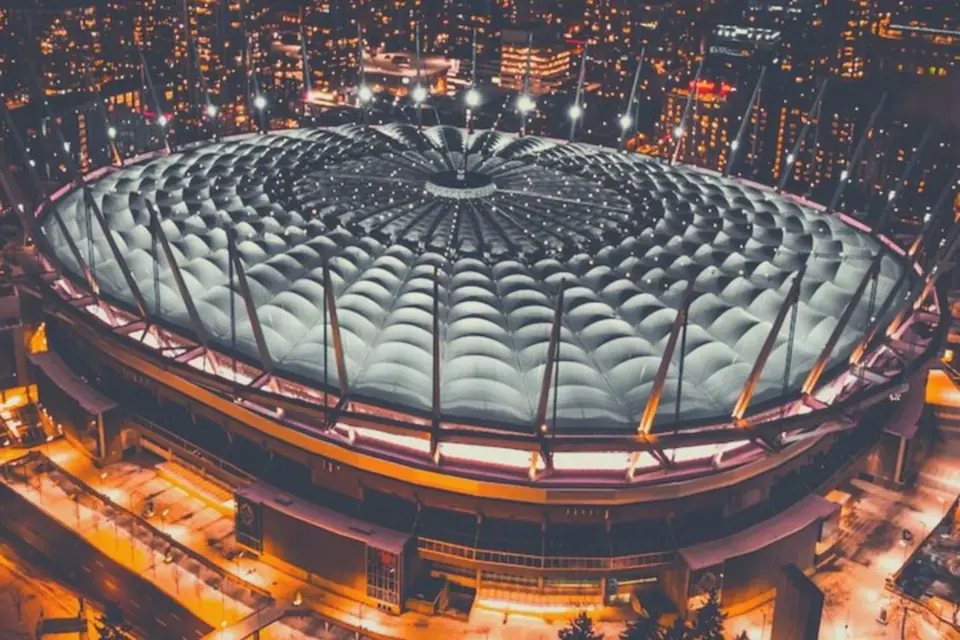 Aerial night view of Vancouver's BC Place Stadium, brilliantly illuminated, showcasing its modern architecture amidst city lights, perfect for an exciting Vancouver Whitecaps MLS match experience.