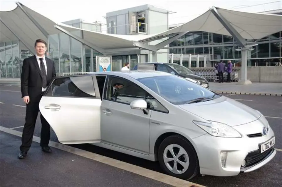 穿西裝的專業司機在倫敦希斯洛機場外，打開銀色私家車門，準備迎接搭乘包車接送服務的旅客。