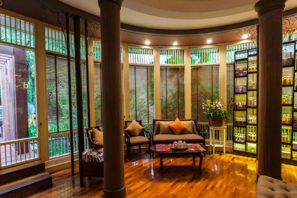 The reception area of DIVANA DIVINE Spa in Bangkok, with comfortable seating surrounding wooden pillars and shelves displaying a variety of signature spa products, showcasing rustic design.
