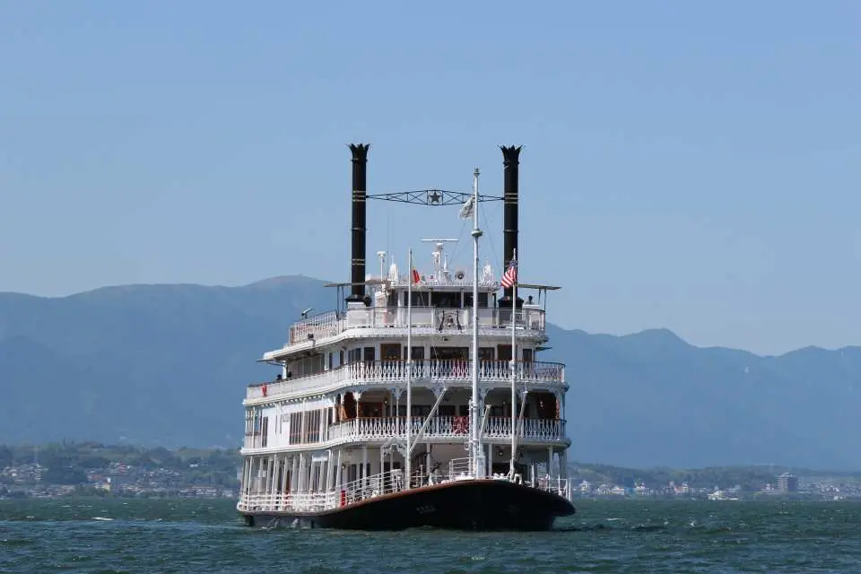 A vintage sightseeing boat cruising on Lake Biwa under a clear sky, with rolling mountains in the background, offering a relaxing experience of the lake's natural beauty.