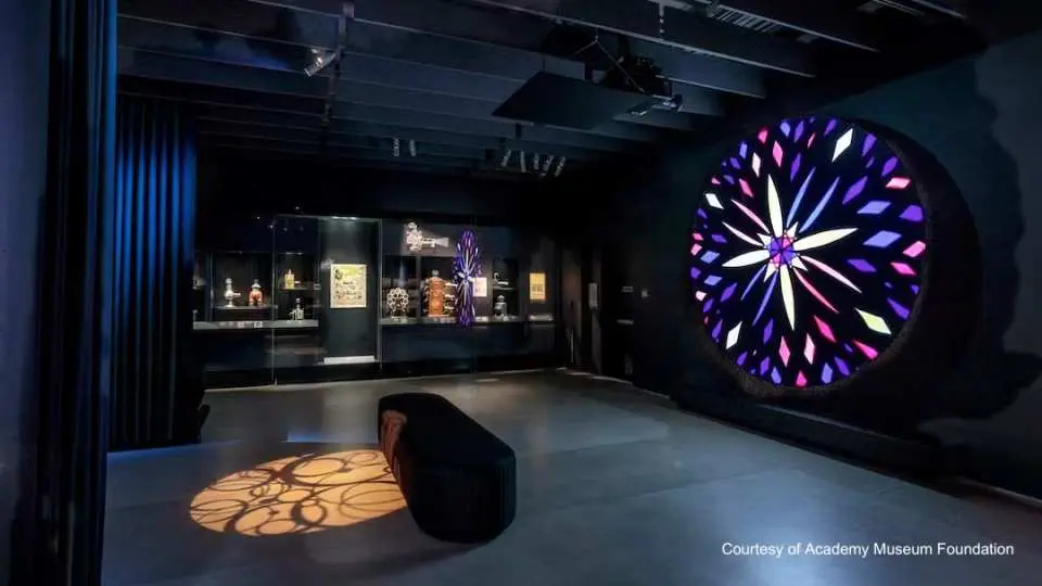 オスカー映画博物館の没入型照明アート展示エリア。巨大なカラフルな円形装置が暗闇で輝き、床には魅力的なパターンが投影されています。