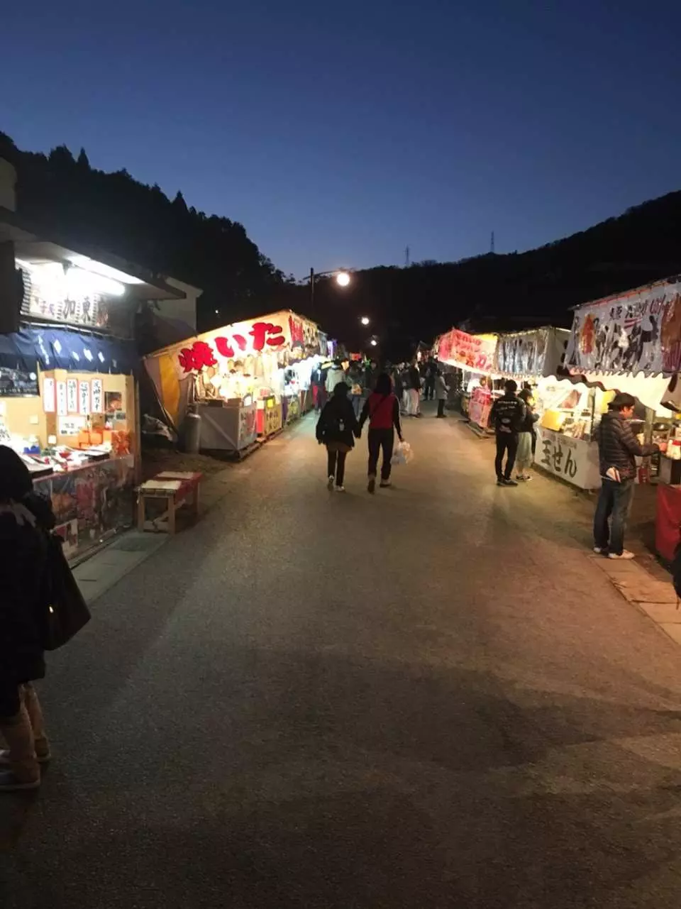 The lively night market during Nagoya Korankei's night maple illumination, with illuminated food stalls lining the path, offering visitors delicious local snacks and a festive autumn evening atmosphere.
