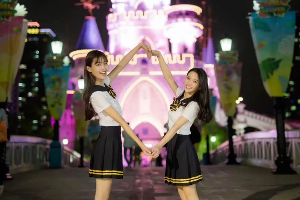兩位少女在韓國首爾樂天世界城堡的璀璨夜景前，穿著梨花校服，手比愛心，留下浪漫的旅行足跡。