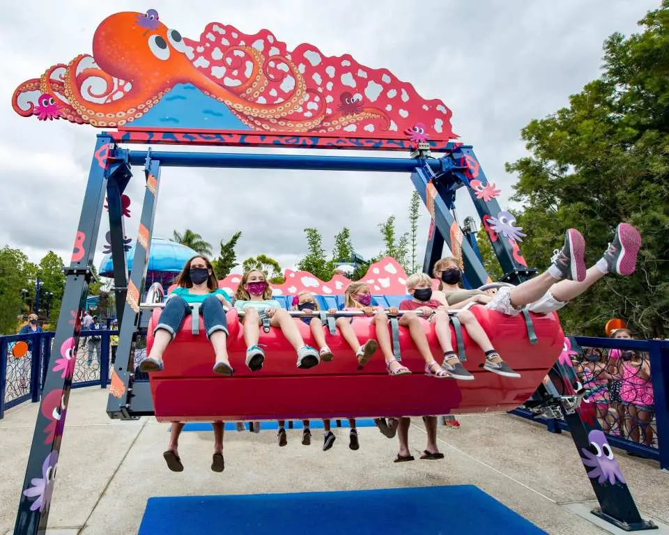 Children happily enjoying an octopus-themed swing ride at San Diego SeaWorld, with masked kids delighting in the gentle spinning motion, a fun family attraction within the park.