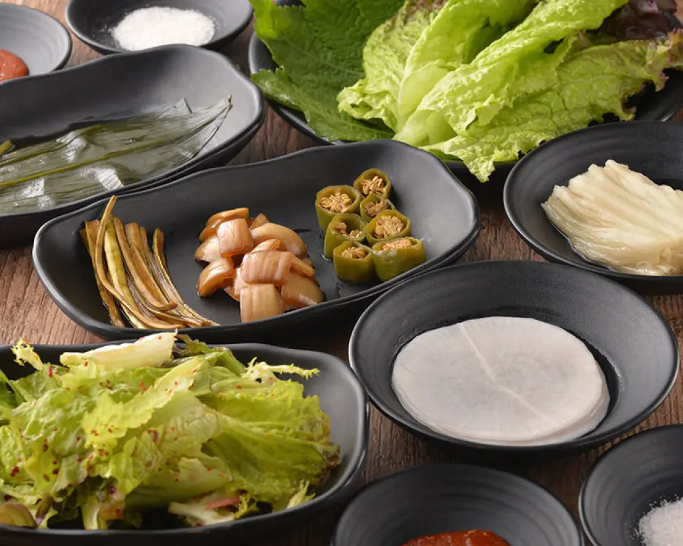 숙성육의 맛을 극대화하기 위해, 우리는 또한 그것과 함께 제공되는 양념에도 많은 신경을 썼습니다. 우리는 여섯 가지 다른 양념을 제공합니다! 명기나물, 마늘싹, 양파, 고춧가루(약간 매운맛), 백김치(숙성김치), 무(달콤하고 신맛) 그리고 건강한 식사를 위한 많은 야채! 그 중에서도 명기나물은 결코 질리지 않는 상큼한 맛으로 고객들에게 인기가 많습니다. 그것을 먹는 가장 좋아하는 방법을 발견하세요!