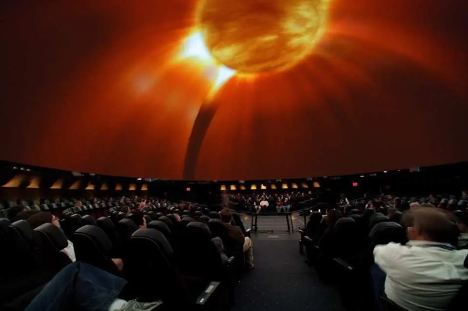 Audience inside the Hayden Planetarium watching an immersive space show, with a giant dome screen displaying solar system and cosmic wonders.
