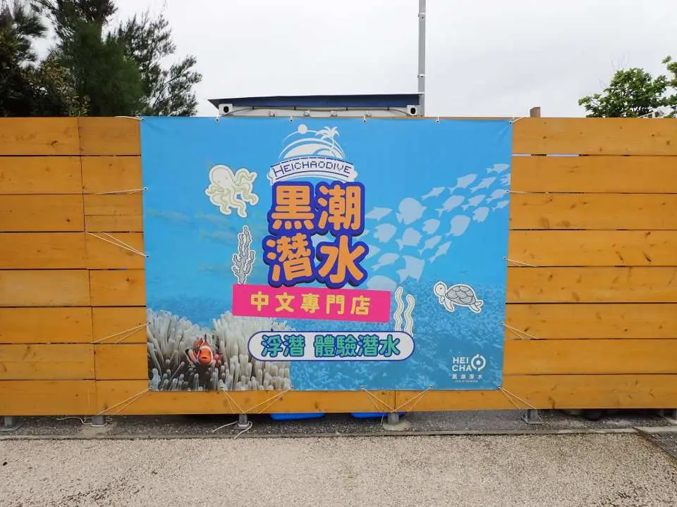 沖縄の「黒潮ダイブ」中国語専門店の看板。木製の壁に設置され、シュノーケリングと体験ダイビングサービスを提供し、観光客を案内しています。