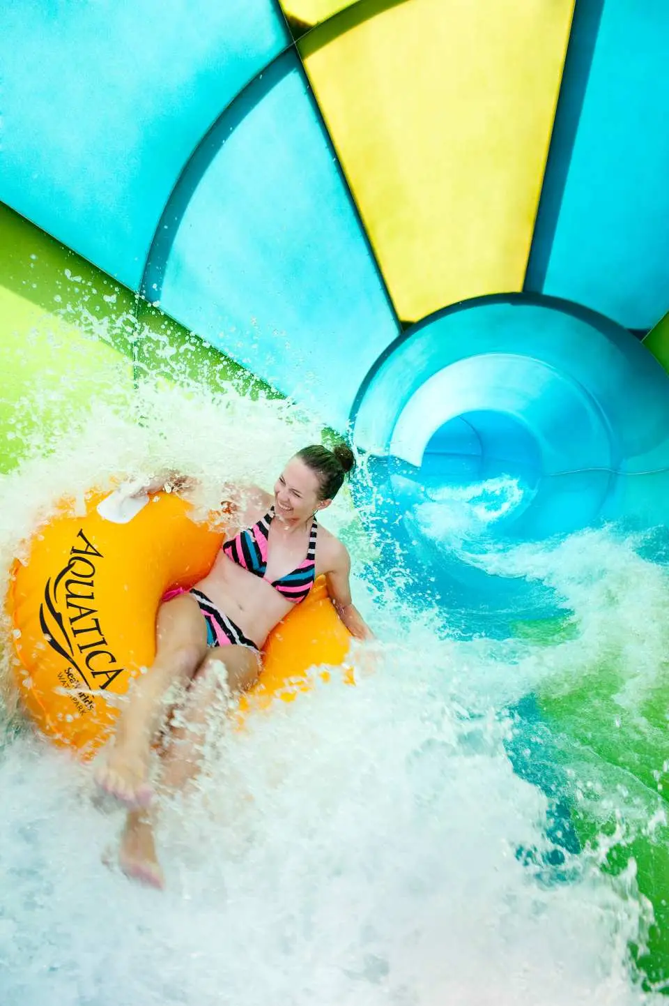 A smiling visitor on a donut-shaped inner tube, rapidly sliding down a colorful water slide at Aquatica Orlando or Adventure Island, enjoying the splash.