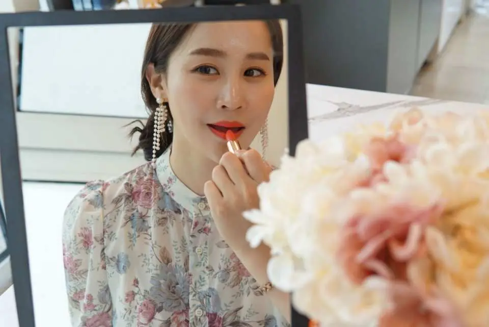 After a Korean beauty DIY class, a participant applies her handmade lipstick in the mirror, showcasing makeup application and the practical use of customized beauty products.
