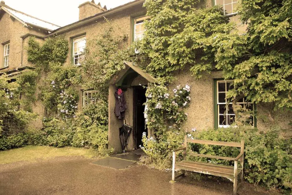 The charming ivy-clad exterior of Lindeth Howe Country Hotel, Beatrix Potter's former home, with a wooden bench and flowering plants, perfect for enjoying a delightful English afternoon tea.