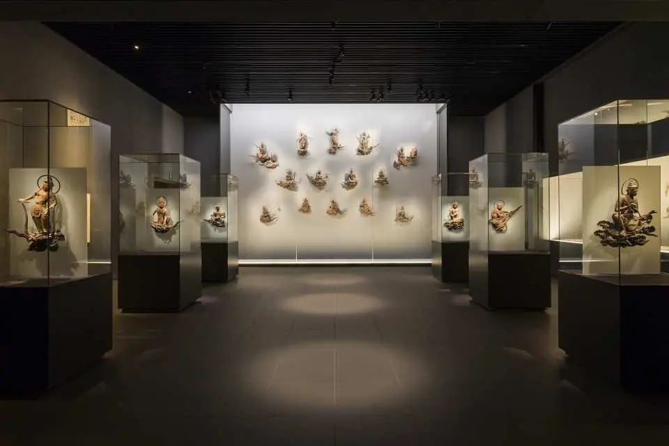 平等院鳳翔館の内部。多数の精巧な仏像や国宝が現代的な展示ケースに並び、夜間拝観の訪問者向けに美しくライトアップされています。