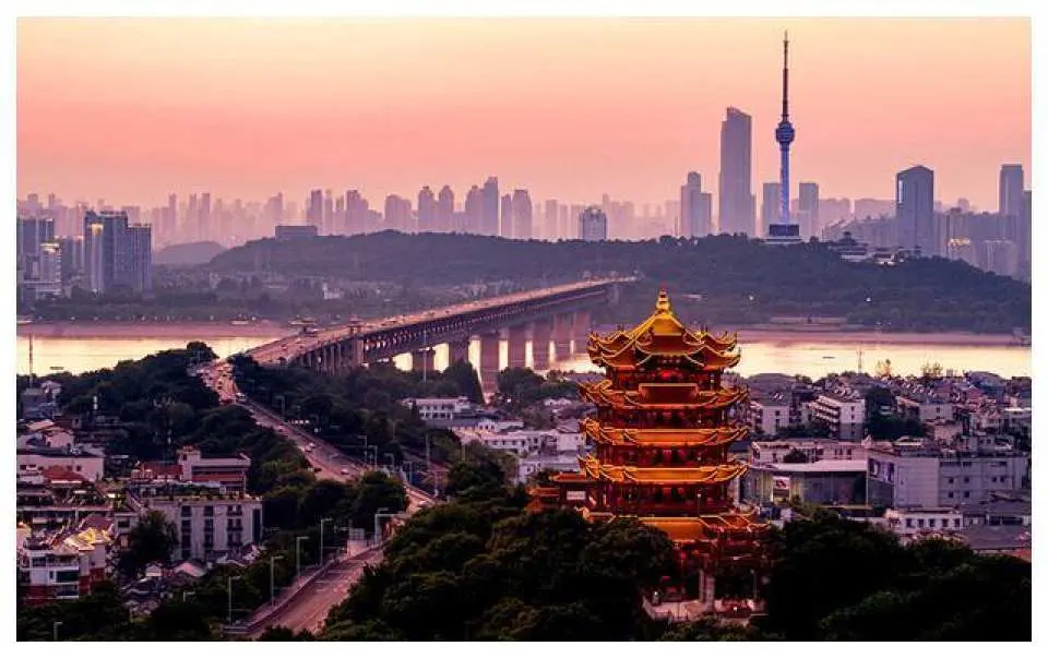 武漢黃鶴樓在黃昏時分的壯麗景色，橙紅色天空映襯著古老樓閣與現代城市天際線和長江大橋。