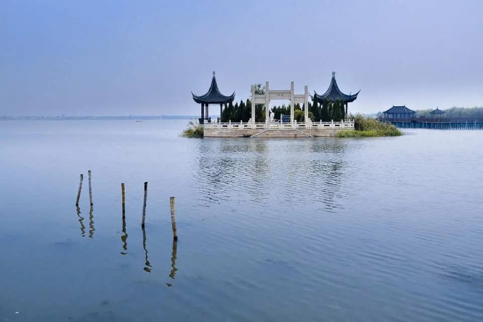 武漢東湖寧靜的湖面風光，一座傳統中式涼亭在湖心小島上，周圍環繞著綠樹與水生植物，景色宜人。