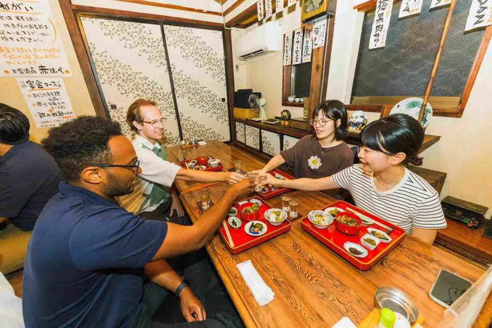 International travelers on the Jionji Temple spiritual culture tour raise a toast in a traditional Japanese room, enjoying a moment of cultural exchange and camaraderie.