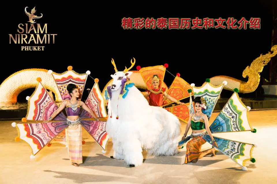 Dancers in magnificent costumes with fan-shaped props performing alongside a white mythical creature on Siam Niramit Phuket's stage, vividly interpreting Thai history and culture.