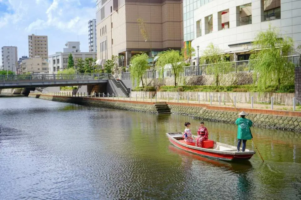 日本福岡博多川泛舟遊船，船夫撐篙載著兩位身穿和服的乘客，沿著河岸巡禮，享受城市與自然交織的歷史水路風光。