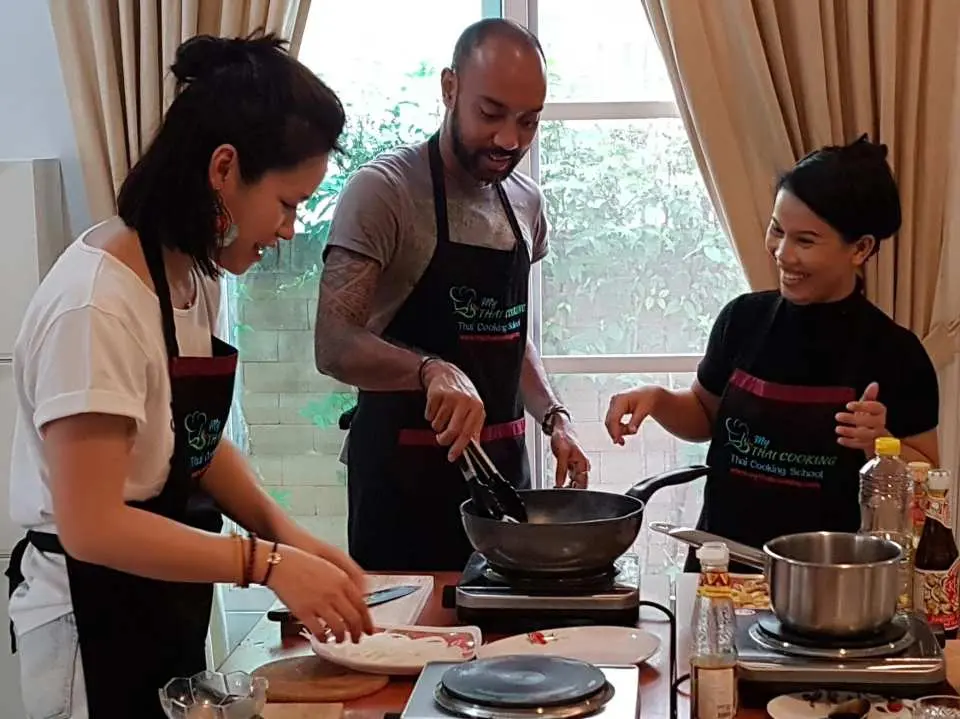 Students happily learning practical Thai cooking techniques under instructor guidance in the home-style kitchen of My Thai Cooking school in Bangkok.