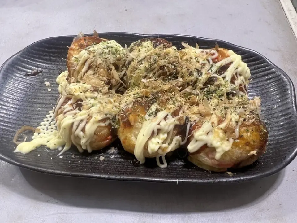 大阪店員烤製的章魚燒熱氣騰騰，鰹魚碎飛舞，外脆內軟，展現關西地道風味！共有六種不同口味可供選擇，其中最受歡迎的是經典的“蛋黃醬醬”，這是濃鬱的醬汁和溫和的蛋黃醬的完美結合。搭配您最喜歡的配料一起享用，例如明太子醬或起司咖哩。我們還提供小吃、油炸食品和米飯。我們也提供外帶服務，讓您在家就能享用我們的美食！