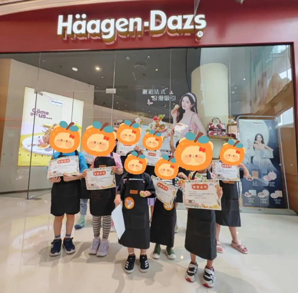 Trải nghiệm nghề nghiệp cho trẻ em ở Thâm Quyến, các nhà sáng tạo kem nhỏ mặc đồng phục Häagen-Dazs, cầm giấy chứng nhận, vui vẻ chụp ảnh trước cửa hàng Häagen-Dazs.