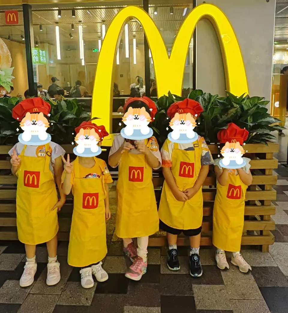 Trong hoạt động trải nghiệm nghề nghiệp cho trẻ em ở Thâm Quyến, một nhóm trẻ em mặc đồng phục McDonald's, hóa thân thành nhân viên phục vụ nhỏ, vui vẻ chụp ảnh trước logo chữ M khổng lồ.
