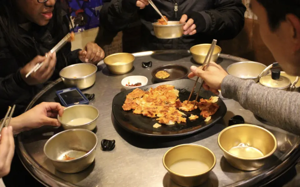 小團旅客們在首爾夜間美食之旅中，共享美味的韓國煎餅、泡菜等傳統小吃，並嘗試搭配特有酒精飲料。