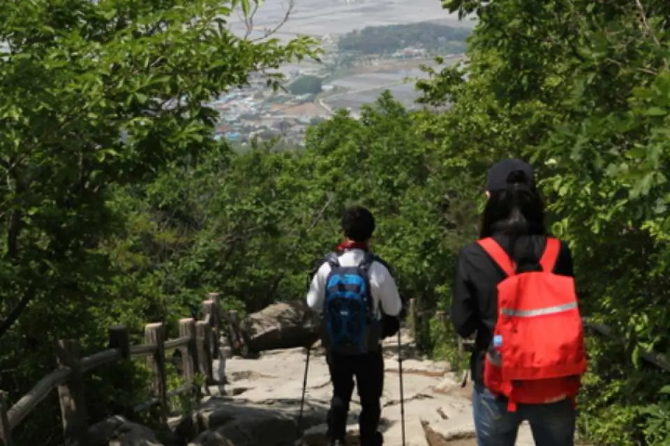 两位登山客在摩尼山健行步道上，背对镜头远眺江华岛风景，享受大自然户外探险的乐趣。
