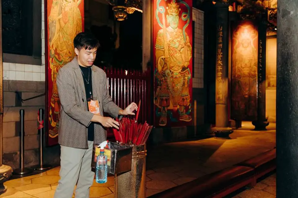 An English-speaking guide demonstrates incense offering at Taipei's Longshan Temple, explaining unique Taiwanese temple culture to visitors.