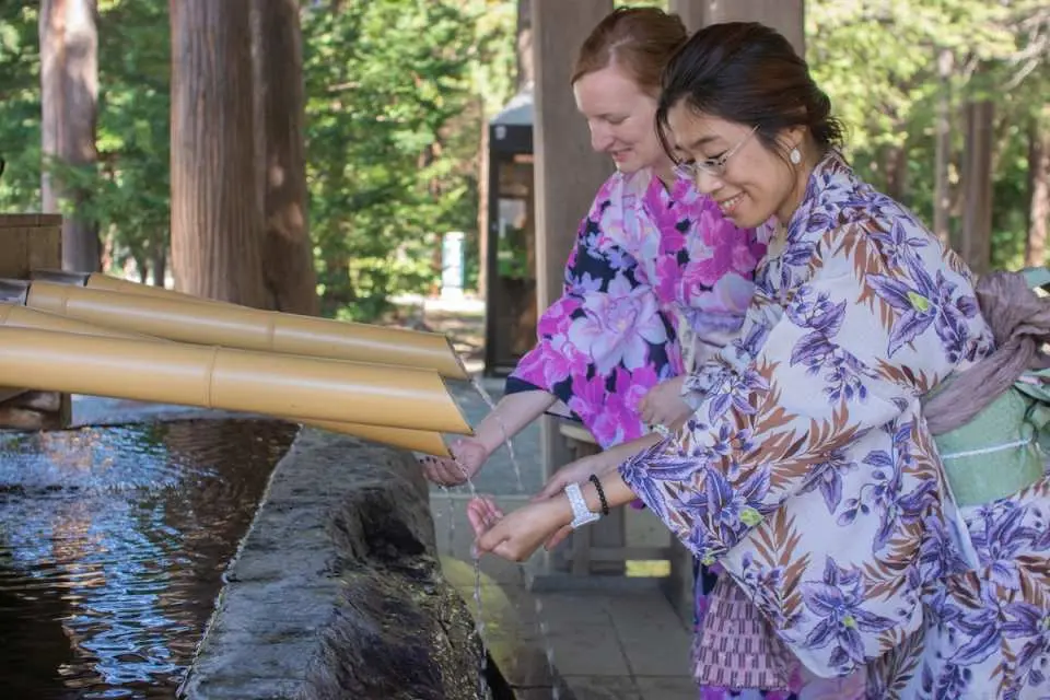 Two kimono-clad visitors performing a purification ritual at Hokkaido Shrine's chozuya in Sapporo, embracing traditional Japanese customs.