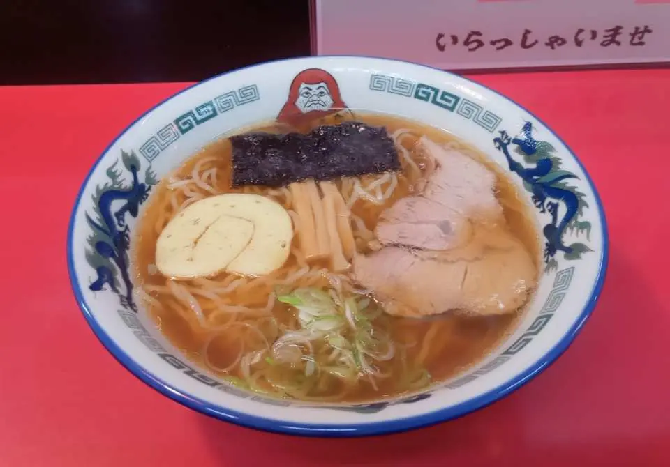 A classic Sapporo ramen bowl, richly topped with thick chashu, soft-boiled egg, seaweed, and green onions, served in an exquisite bowl with a Daruma design, a visual delight for the ultimate ramen experience.