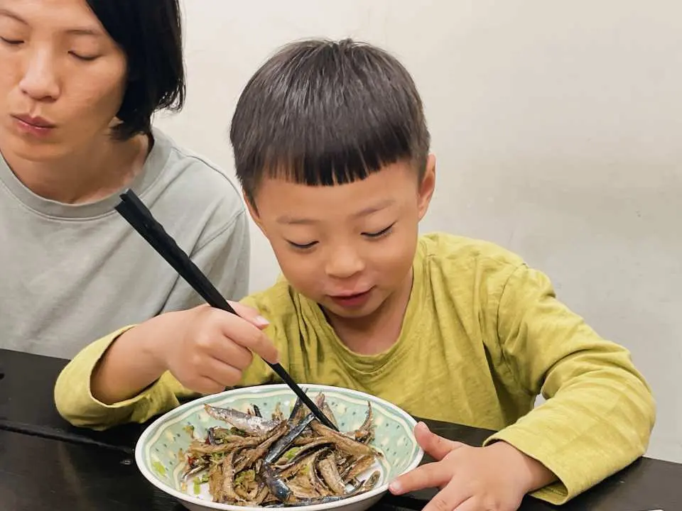 澎湖敲魚乾體驗的品嚐環節，小男孩興奮地用筷子夾起碗中處理好的魚乾，展現親子同樂、享用在地美食的快樂時光。