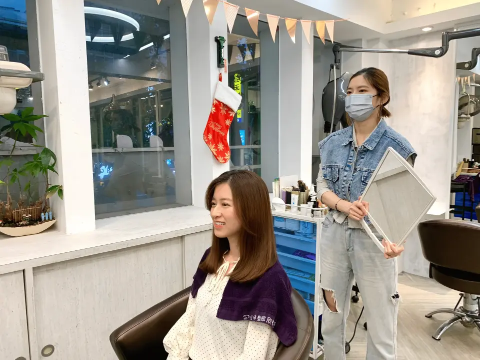 顧客在台北小林美髮沙龍完成台灣坐式洗髮後，美髮師拿鏡子讓她檢視成果，臉上洋溢著滿意的笑容，髮型清爽亮麗。