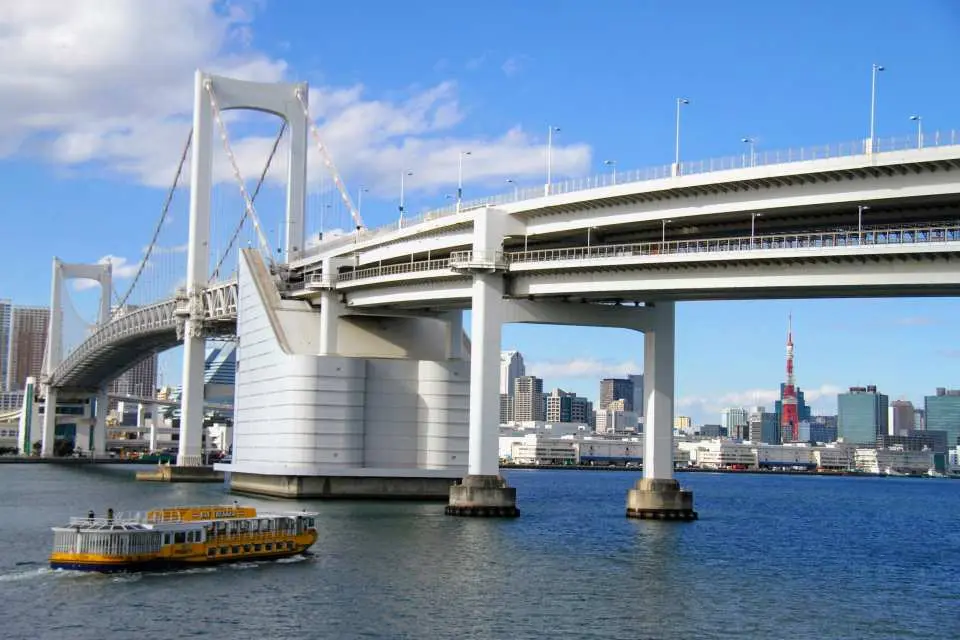 Majestic Rainbow Bridge from a Tokyo Bay cruise perspective, with a ferry passing and the magnificent Tokyo cityscape and Tokyo Tower in the background.