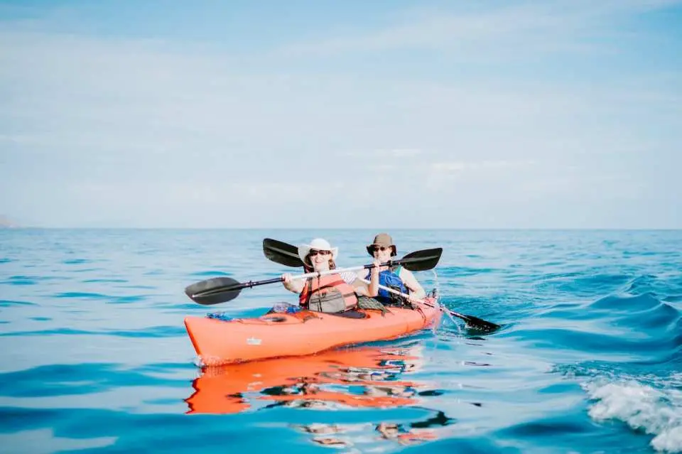 Two tourists in an orange double kayak paddle on the clear blue waters of Labuan Bajo, enjoying a scenic adventure within Komodo National Park, Indonesia.