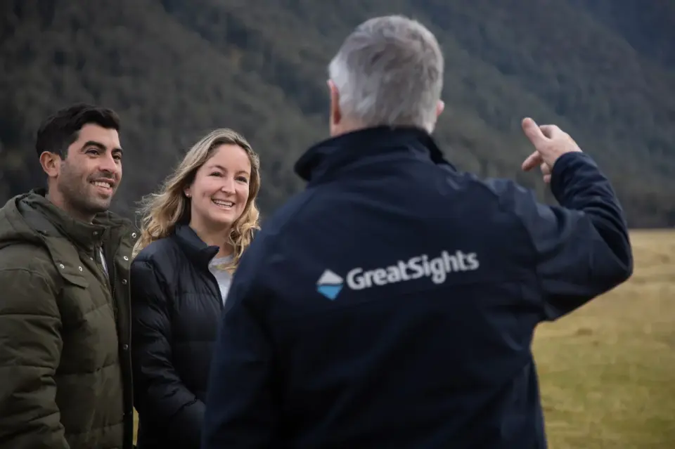 Happy tourists engaging with a knowledgeable GreatSights guide, pointing out sights during the scenic bus tour to Milford Sound, enhancing the educational experience.
