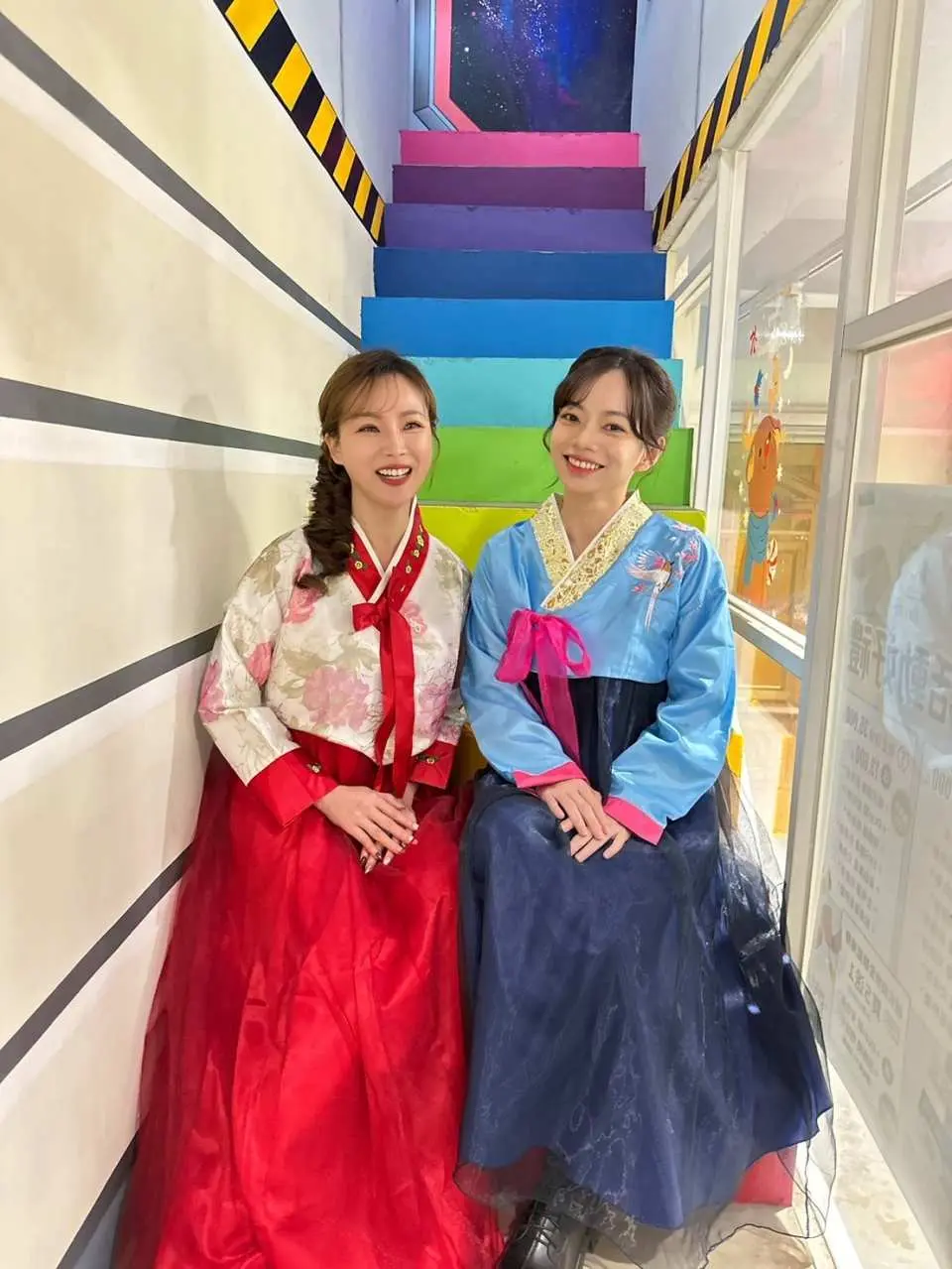 台北西门町韩服体验，两位顾客穿着亮丽韩服，在彩虹楼梯前开心合影，享受闺蜜变装乐趣。