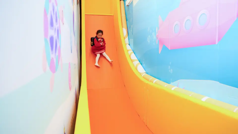 Children happily sliding down the wide orange slide at Sunday Island Playhouse, surrounded by an underwater-themed wall, enjoying an exciting and immersive experience.