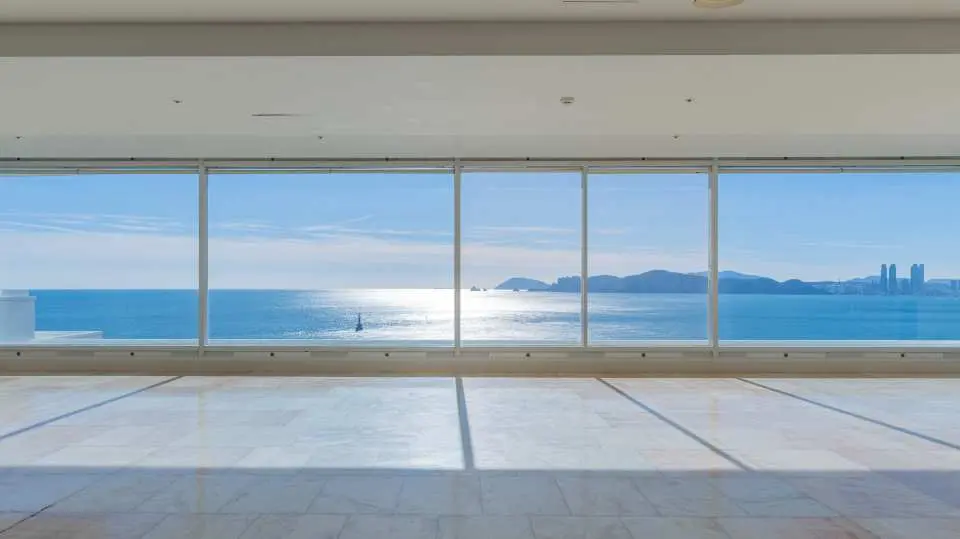 Another spacious and bright viewing area at Busan Haeundae HILL SPA, where sunlight from Haeundae fills the room through floor-to-ceiling windows, revealing expansive ocean views and cityscapes in the distance.