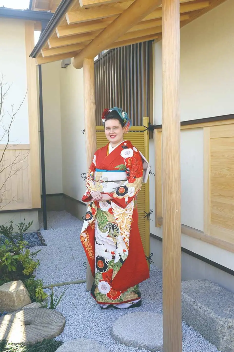 A lady in a vibrant red traditional kimono showcased at the entrance of a Japanese garden in Kisarazu, Chiba, highlighting beautiful patterns for photography.