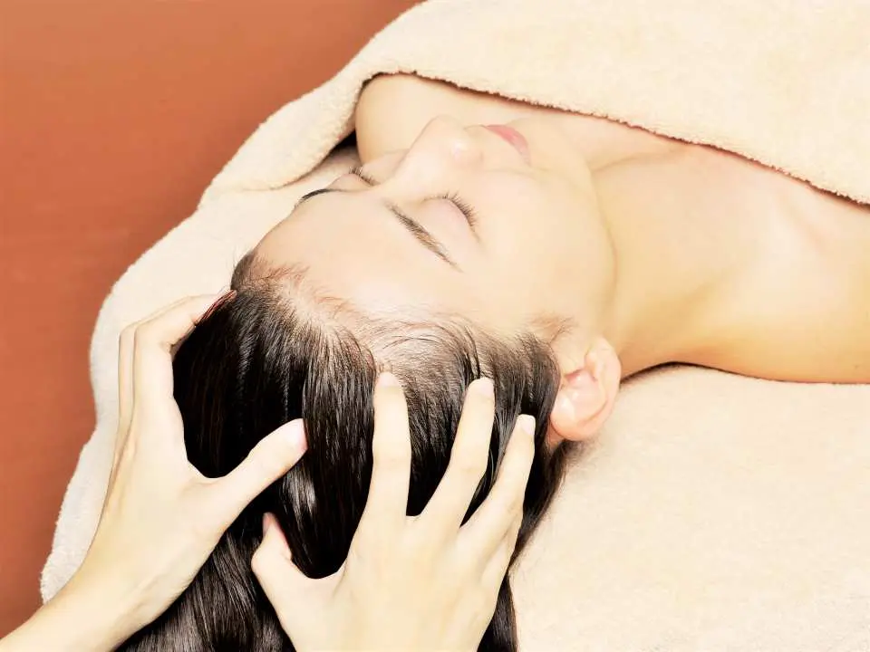 An aesthetician performing a soothing scalp massage for a client at a Ginza, Tokyo salon, easing stress, promoting head circulation, and delivering an ultimate relaxation experience.