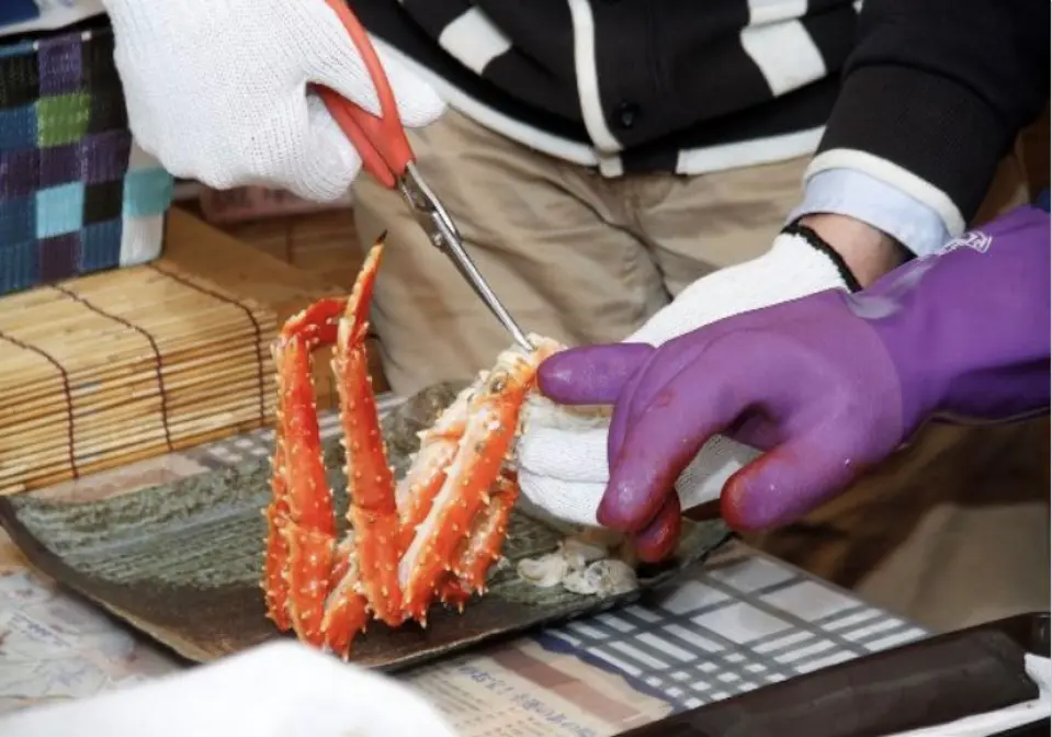 An artisan in Abashiri, Hokkaido, meticulously demonstrates crab cutting techniques, using scissors to precisely section a cooked crab leg, guiding guests on how to easily extract the flavorful meat.